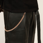 ICED London rose-gold chain accessory clipped to black leather pants, close-up.
