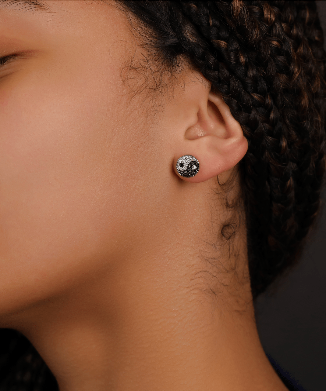 ICED London yin-yang stud earring on a woman's ear; silver with black and white crystals, close-up jewelry photo.